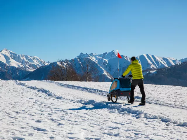 Wandelaar in de bergen die een kinderwagen in de sneeuw voortduwt