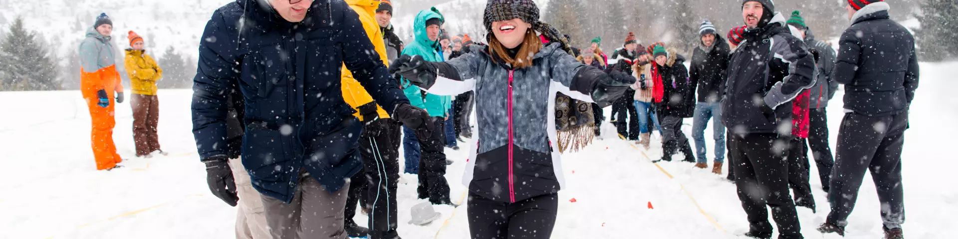 group of young happy business people having a Blindfolded games competition while enjoying snowy winter day with snowflakes around them during a team building in the mountain forest