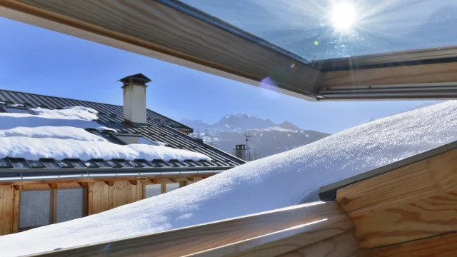 uitzicht vanuit een openslaand raam op een dak bedekt met sneeuw in een alpenhuisje